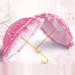 Parapluie canne élégant rose avec volants, armature dorée, style raffiné, devant un fond floral pastel pour une touche chic.