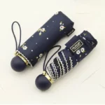Parapluie femme léger pliant bleu marine avec motifs floraux blancs, compact et facile à transporter grâce à sa poignée ronde.