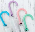 Parapluie transparent fleuri, poignées colorées bleu, violet, rose, vert, collection élégante sur fond bois clair.