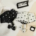 Parapluies pliants anti-UV à pois noirs et blancs avec serre-têtes assortis, affichés sur fond texturé avec calendrier 13 juin.