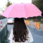 Parapluie femme coloré rose, chic et tendance, parfait pour la pluie, vu de dos dans une rue avec des bloques-route arrière.