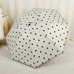 Parapluie anti-UV pliant élégant à pois noirs sur fond blanc, pratique et stylé, parfait pour se protéger de la pluie et du soleil.