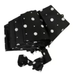 Parapluie anti UV pliant, noir à pois blancs avec nœud assorti, élégant et pratique pour une protection solaire optimale.