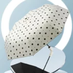 Parapluie anti-UV pliant élégant à pois noirs sur fond beige, design moderne et pratique, idéal pour se protéger du soleil et de la pluie.
