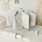 Parapluie automatique fleuri, élégant et moderne, motif floral sur fond gris, accessoire chic posé avec étui assorti.