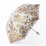 Parapluie de luxe en dentelle, motif floral doré et argenté, accessoire élégant et raffiné pour un style sophistiqué sous la pluie.