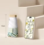 Parapluie compact vintage floral, design printanier élégant, posé à côté d’un smartphone sur un fond neutre, hauteur 14 cm.