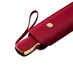 Parapluie de luxe minimaliste avec étui rouge élégant, bouton doré et anse pratique, parfait pour un style raffiné et fonctionnel.