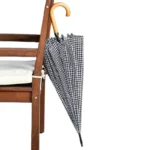 Parapluie élégant à motifs noir et blanc suspendu à une chaise en bois, accessoire chic et pratique pour affronter la pluie.