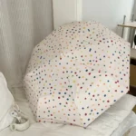 Parapluie femme à pois colorés sur un lit, accessoire élégant et joyeux, idéal pour affronter la pluie avec style.