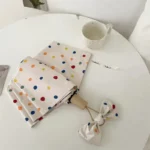Parapluie femme à pois colorés sur table avec accessoire assorti et tasse, parfait pour une protection élégante contre la pluie.