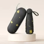 Parapluie femme compact noir avec motifs cœurs jaunes, élégant et pratique, incluant un étui de rangement sur fond neutre.