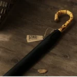 Parapluie homme canne en bambou avec poignée courbée, revêtement noir élégant, posé sur sol bois, étiquettes vintage