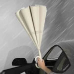 Parapluie inversé pastel beige, protection élégante contre la pluie, tenu à travers une fenêtre de voiture sous une averse.