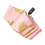 Parapluie pliant rose à motif feuilles dorées, poignée noire élégante, compact et tendance pour une protection stylée.