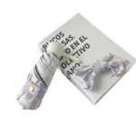 Parapluie pliant violet avec motif floral pastel et nœud assorti, posé élégamment sur un livre avec inscriptions noires.