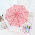 Parapluie transparent décoré de fleurs roses ouvert, tubes colorés à côté sur une table, élégant et pratique pour une touche printanière.