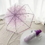 Parapluie transparent fleuri avec fleurs violettes, poignée droite, ouvert sur surface claire, bouteille violette en décor.