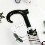 Canne parapluie noire élégante avec béquille antidérapante, design pratique, entourée de végétation et décorations festives.