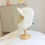 Capuche de pluie chaude blanche avec rabats latéraux et cordons, présentée sur un support en bois, [Collection].