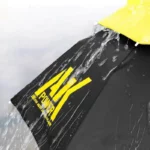 Chapeau parapluie noir de la collection [Collection], avec inscription jaune, illustrant son imperméabilité et résistance à la pluie.