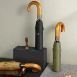Parapluie homme pliant élégant avec poignée en bois, disponible en noir, vert et beige, parfait pour un style raffiné et moderne.