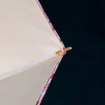 Parapluie luxe fleuri avec attache dorée, couture rouge élégante et toile beige, accessoire chic pour toutes les saisons.