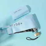 Mini parapluie léger bleu avec protection UV UPF > 50+, plié avec son étui assorti, présenté sur un fond bleu élégant.