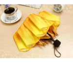 Parapluie original fleur jaune vif plié sur une table en bois, à côté d'une tasse de café, une soucoupe et une horloge rétro.