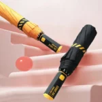 Parapluies pliables anti-retournement modernes, jaune et noir, design élégant sur marches, avec ballon rose pour déco.