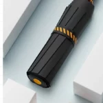 Parapluie anti retournement pliable noir avec motif orange, élégant et compact, présenté sur fond clair avec accessoires blancs.