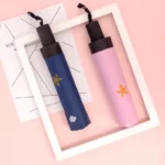 Parapluies compacts design, bleu étoilé et rose, élégamment posés sur fond rose avec cadre blanc, [Collection].