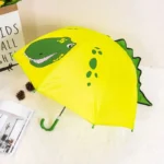 Parapluie enfant coloré avec illustration dinosaure souriant, fond jaune, détails verts et bordure originale en dents noires.