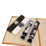 Parapluie femme pliant élégant dans boîte décorative blanche et noire, posé sur un tapis en rotin pour un style raffiné.