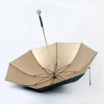 Parapluie luxe doré avec poignée strass élégante, ouvert sur fond blanc, alliant sophistication et protection contre la pluie.