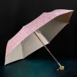 Parapluie luxe fleuri avec motif floral rose élégant, finition intérieure argentée, accessoire chic pour les journées pluvieuses.
