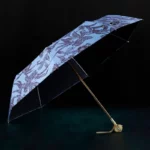 Parapluie luxe rétro avec motif feuilles sur fond bleu, mât doré et poignée décorative, alliant style et protection contre la pluie.
