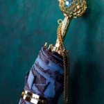 Parapluie luxe rétro, design bleu et doré, accroché à un mur vert, idéal pour allier style raffiné et protection élégante.