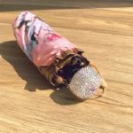 Parapluie luxe rose avec manche doré, poignée strass, motifs floraux, replié et posé élégamment sur une surface en bois.