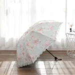 Parapluie mariage brodé, motifs floraux pastel, design élégant, fond bleu clair, sol en bois, lumière douce, collection unique.