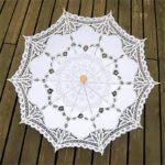 Parapluie mariage en dentelle blanche, élégant et raffiné, parfait pour une cérémonie, posé ouvert sur des planches en bois.