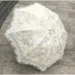 Parapluie mariage vintage en dentelle blanche avec broderies florales, parfait pour une touche élégante lors d'une cérémonie ou photo.
