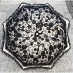 Parapluie mariage vintage en dentelle noire avec motif floral élégant, capturé de dessus sur fond pavé. Accessoire chic et intemporel.