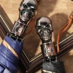 Parapluies originaux à poignées tête de mort, design unique bleu rayé et noir, parfaits pour un style gothique ou élégant.