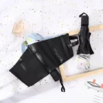 Parapluie pliant fleuri ouvert avec un parapluie noir fermé, sur fond doré scintillant et flacon de parfum élégant.