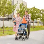 Famille en balade sous le soleil, poussette équipée d'un parapluie clipser orange pour une protection pratique et élégante.