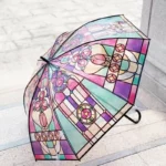 Parapluie transparent motifs vitraux pastel, poignée canne élégante, design [Collection], posé sur sol en pierre.