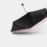 Petit parapluie pliable noir à pois roses, élégant et pratique, accessoire de mode idéal pour un look tendance par temps de pluie.