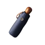 Petit parapluie pliable bleu marine avec poignée en bois et sangle en cuir, pratique et élégant pour une protection contre la pluie.