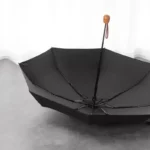 Petit parapluie noir élégant ouvert, structure solide métal, poignée en bois, design raffiné, parfait accessoire intemporel.